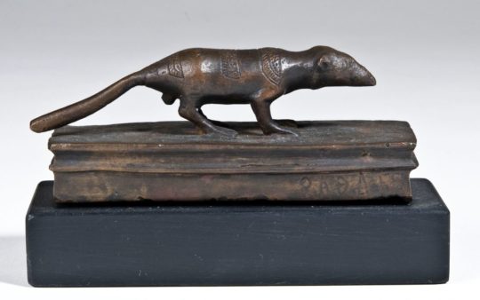 Eine nach rechts gewandte, stehende Spitzmaus aus Bronze mit ausgestrecktem Schwanz, unter ihr ein Bronzeblock.