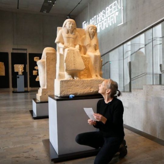 Künstlerin Ruth Geiersberger knieend vor einer altägyptschen Statue