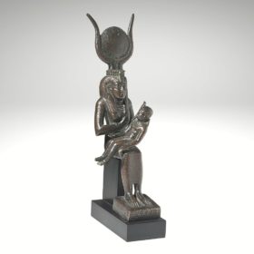 Detailansicht einer Isisstatue aus Bronze. Isis ist in sitzender Haltung egzeigt und hält auf dem Schoß ihren Sohn Horus, dem sie die linke Brust gibt.