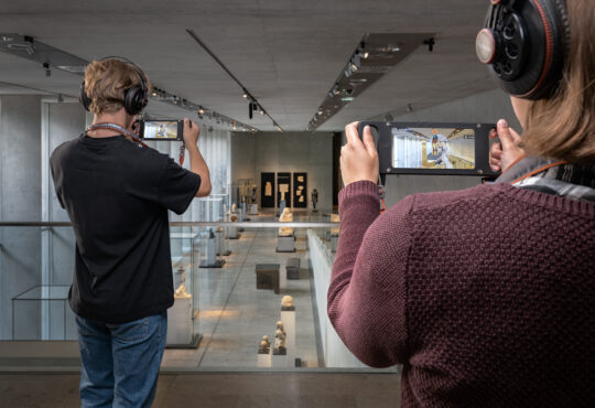 Rückansicht von zwei personen auf der Galerie des Museums, die personen halten das AR-Gerät in den Händen.
