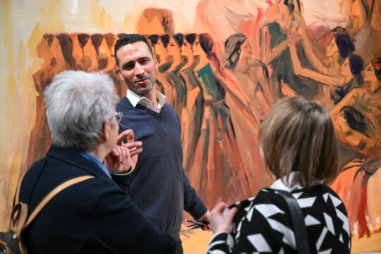 Alaa Awad spricht vor einem Gemälde mit zwei Besucherinnen
