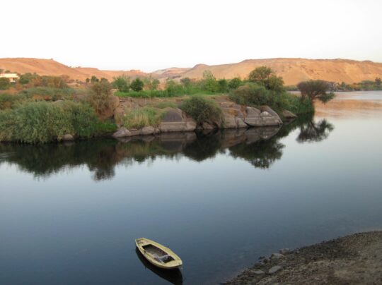 Blick auf den Nil, im Hintergrund rötliche Wüstenberge, im Vordergrund ein vertäutes Boot