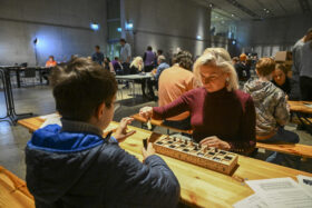 Zwei Personen sitzen an einem Tisch sich gegenüber und spielen Senet.