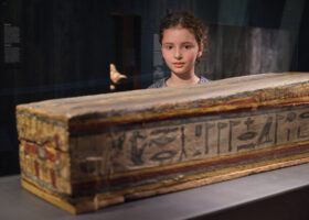 Ein Kind steht hinter einem altägyptischen Sarg