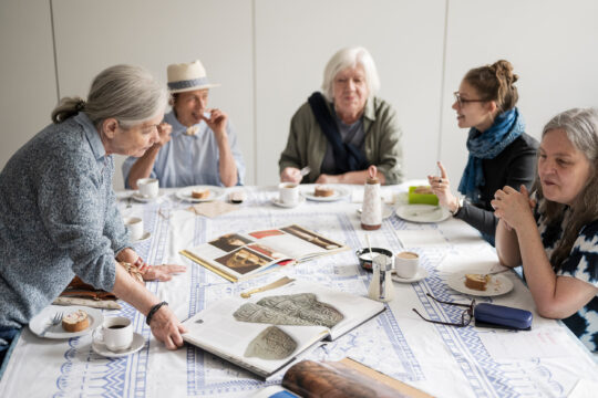 Eine Gruppe älterer menschen sitzt um einen Tisch, unterhält sich und schaut Bücher an.
