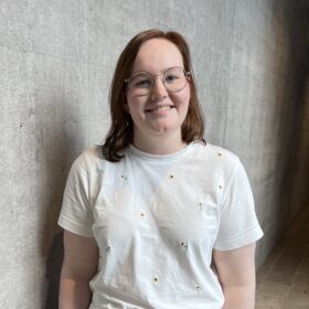 Marie Arnold, eine junge weße Frau mit Brille und braunem Haar, das Glatt bis auf die Schultern fällt.